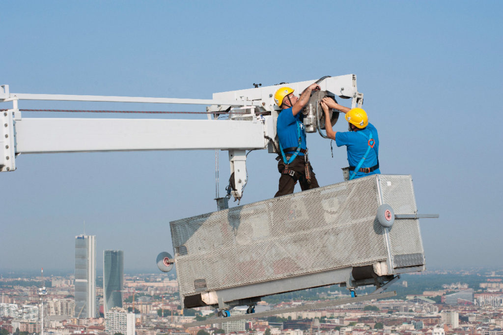 Tecnici al lavoro su piattaforma sospesa per manutenzione in quota di facciate.