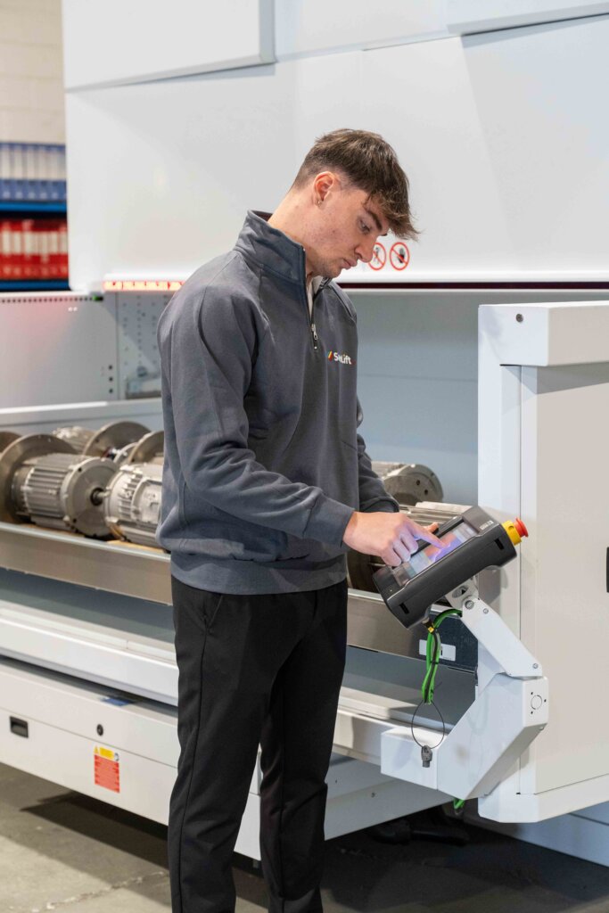 Un giovane tecnico specializzato di SiemLift mentre utilizza una pulsantiera per il controllo e il collaudo di componenti meccanici industriali.