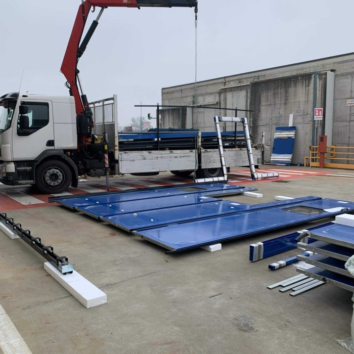 Portone a libro smontato con pannelli blu e camion gru per intervento su chiusura industriale SiemLift.