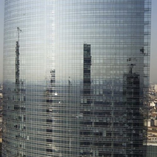Ponteggi motorizzati e sistemi di sollevamento in uso sulla facciata a vetri di un grande edificio.