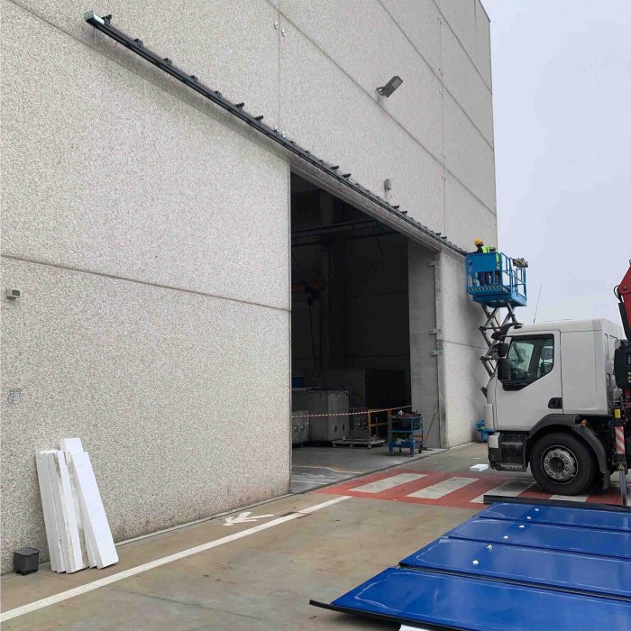 Portone a libro smontato con pannelli blu e camion gru per intervento su chiusura industriale SiemLift.
